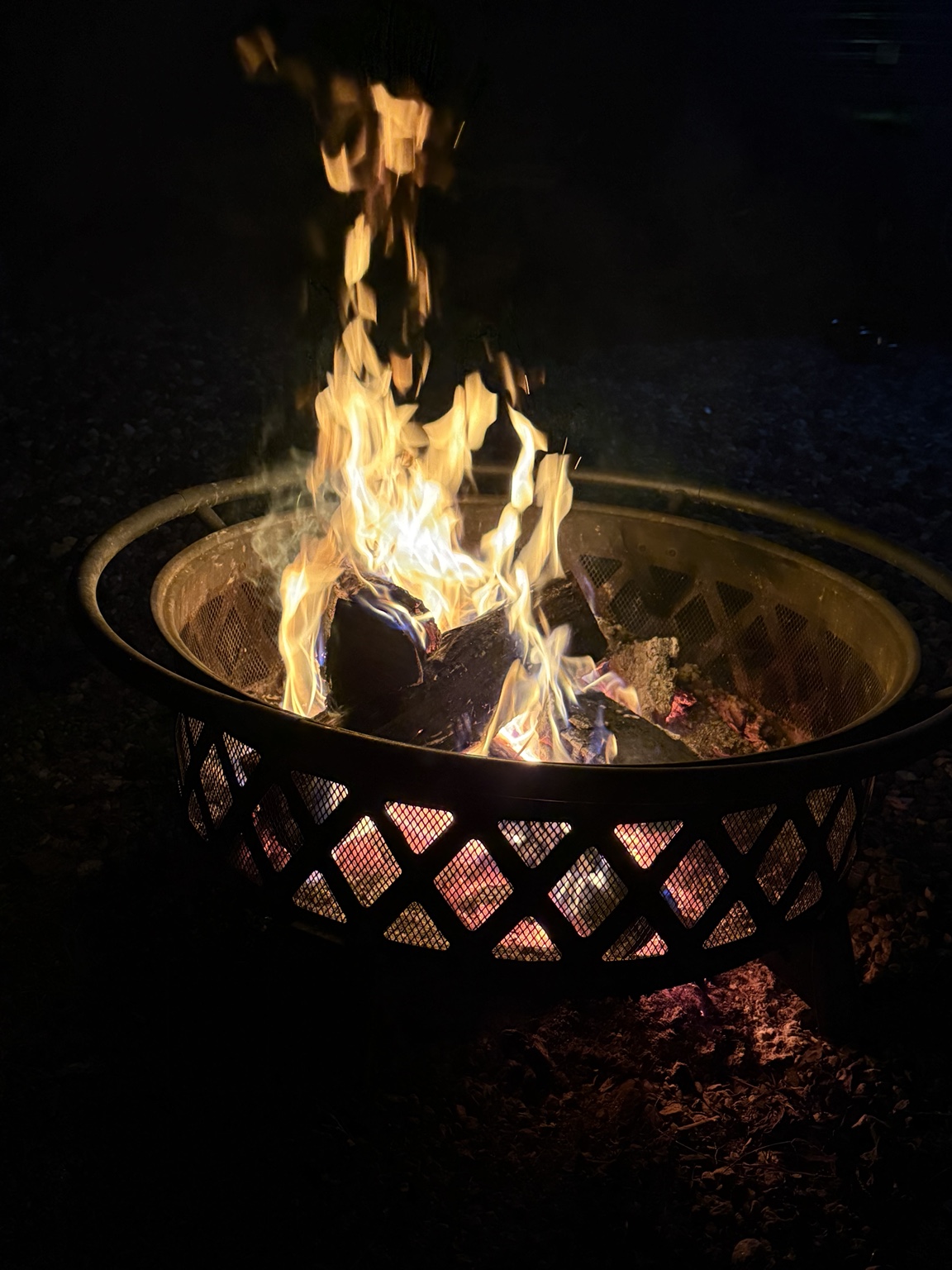A bright campfire burns in a metal fire ring at night, creating a warm place to gather.