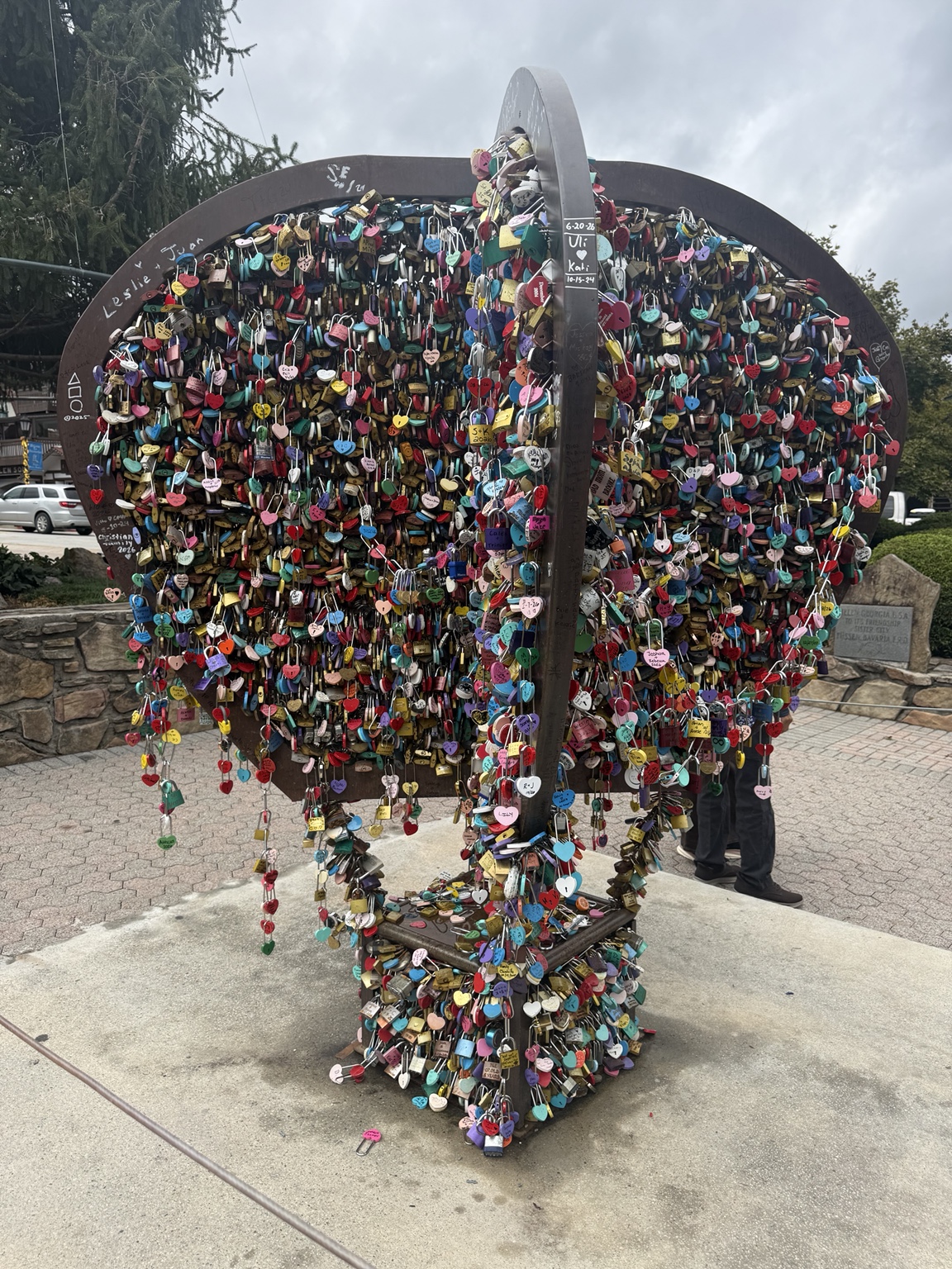 A heart-shaped metal sculpture covered with colorful love locks outdoors.