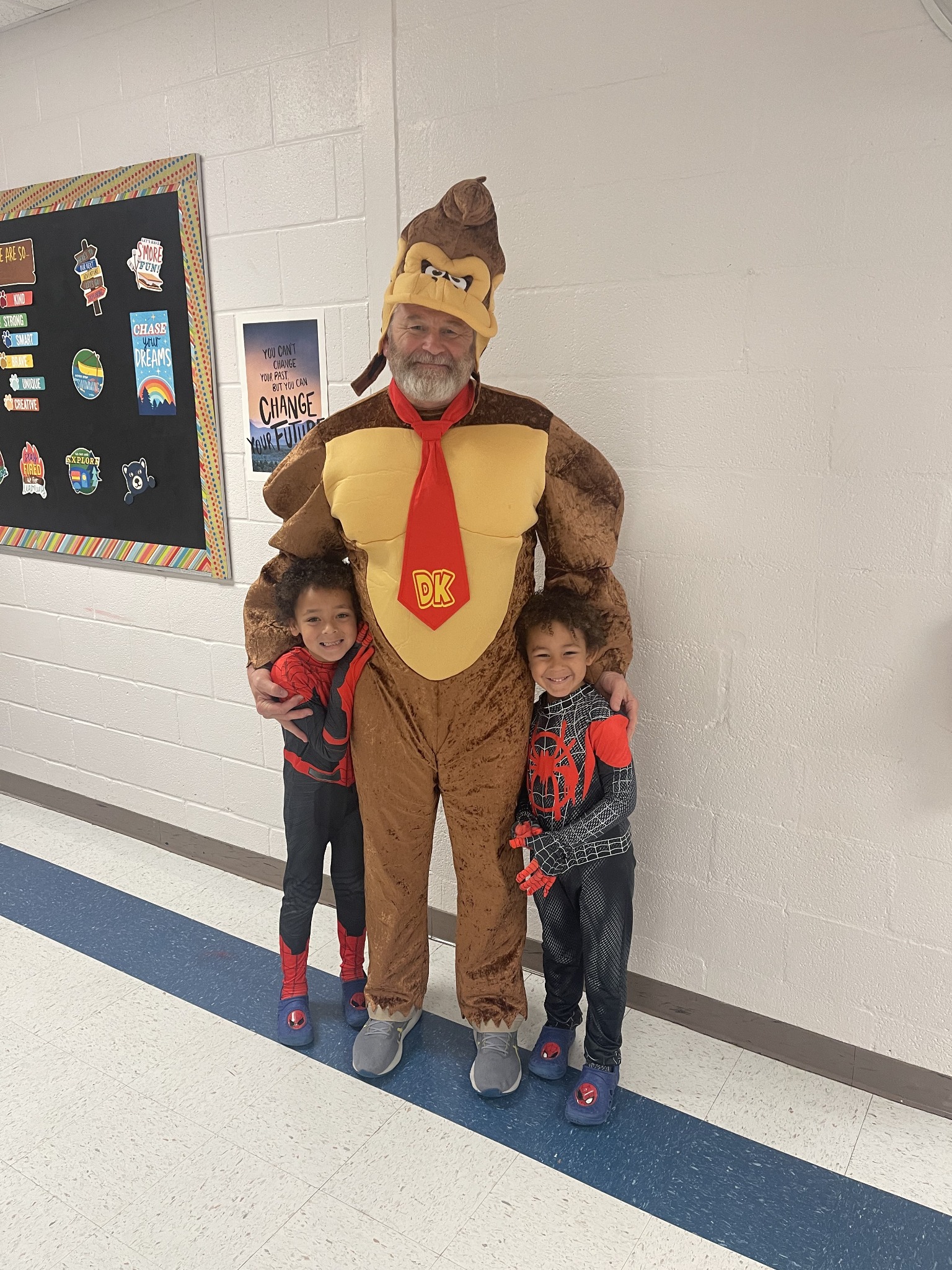 Patrick in a playful Donkey Kong costume standing with two smiling children in superhero costumes.